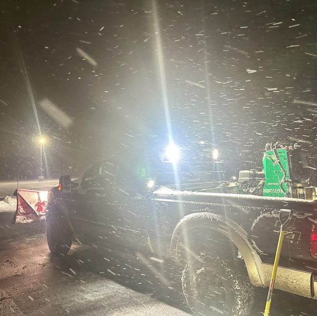 Plow truck working through heavy snowfall after dark
